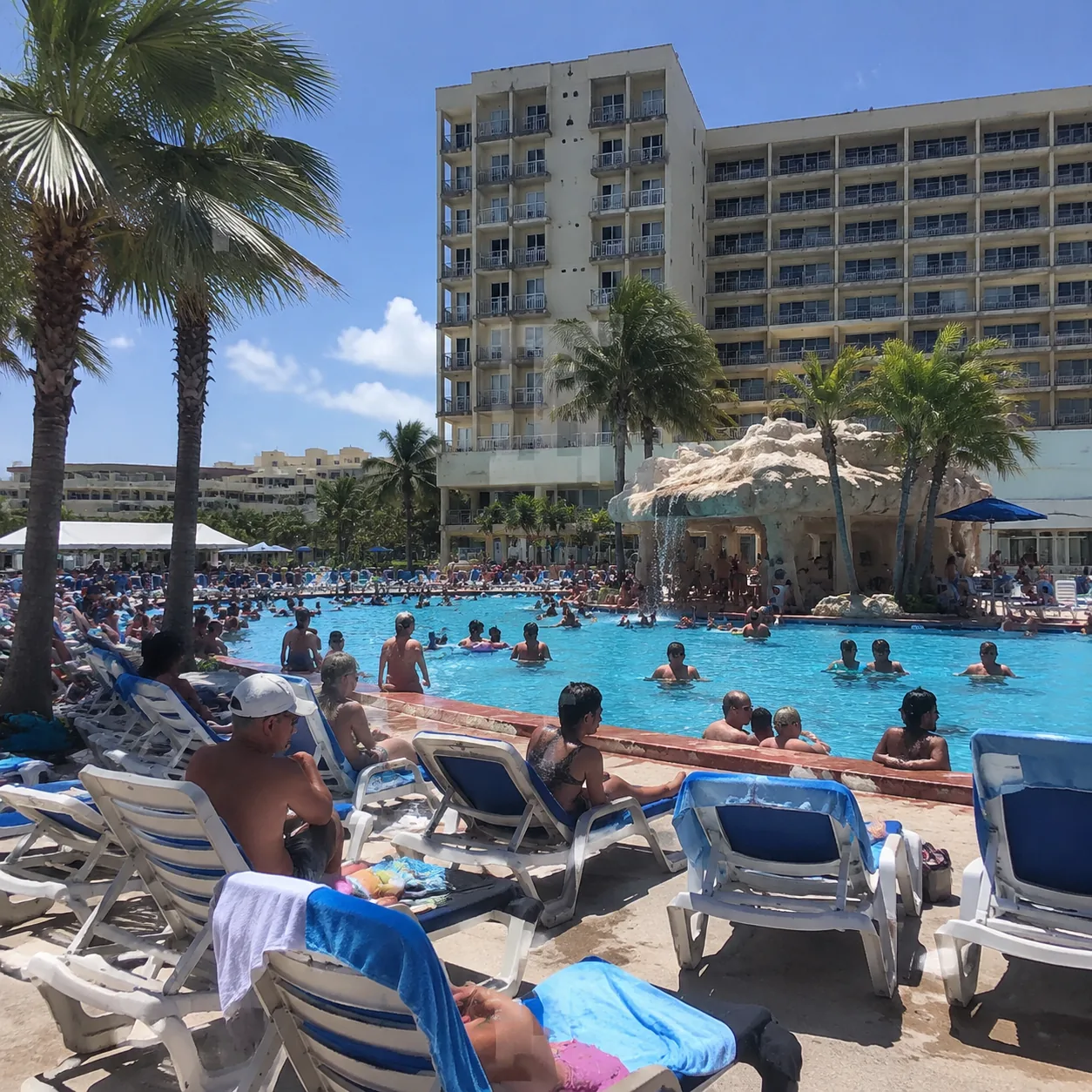 Crowded all-inclusive resort pool on Cable Beach in Nassau Bahamas, rows of plastic loungers, bright midday sun, tired b
