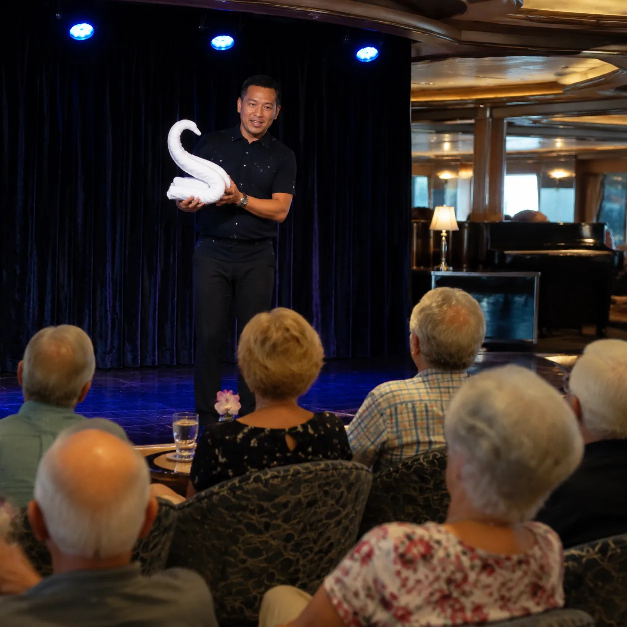 Realistic editorial photo of cruise lounge karaoke setup with microphone, small stage, seated passengers, and warm color