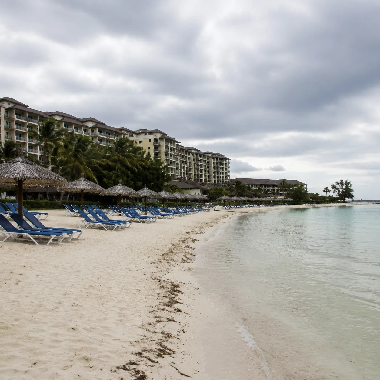 Quiet Grand Bahama resort beach with empty loungers and a large hotel complex behind, overcast sky, calm but underused v