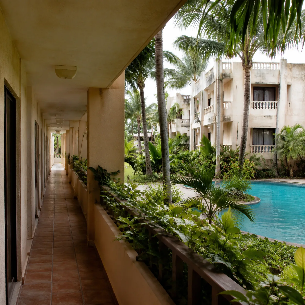 Square editorial travel photo of an adults-only Punta Cana resort hallway and pool, quiet but dated room balconies, humi