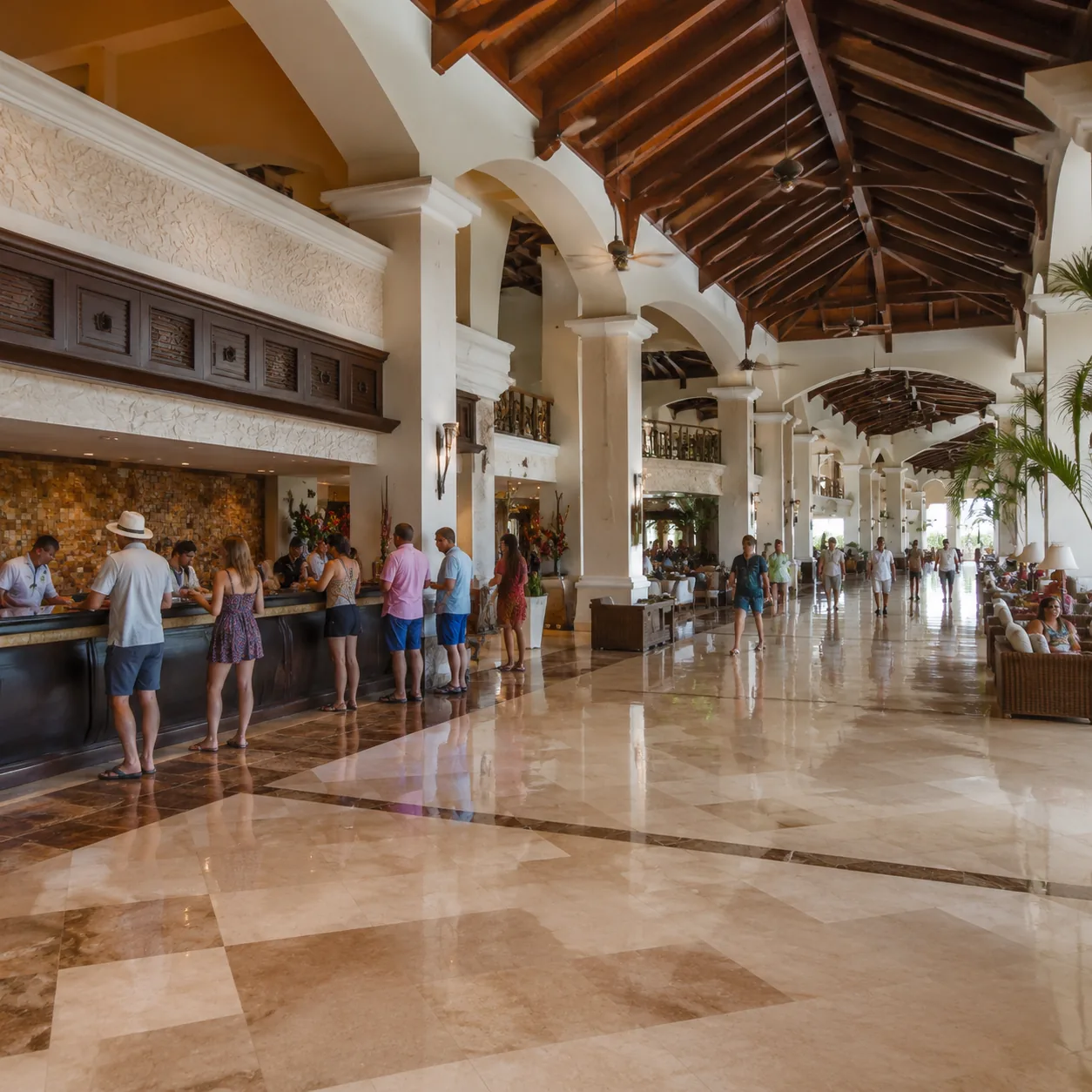 Square photo of a large colonial-style Punta Cana resort lobby, busy check-in desk, long tiled corridors, tropical resor