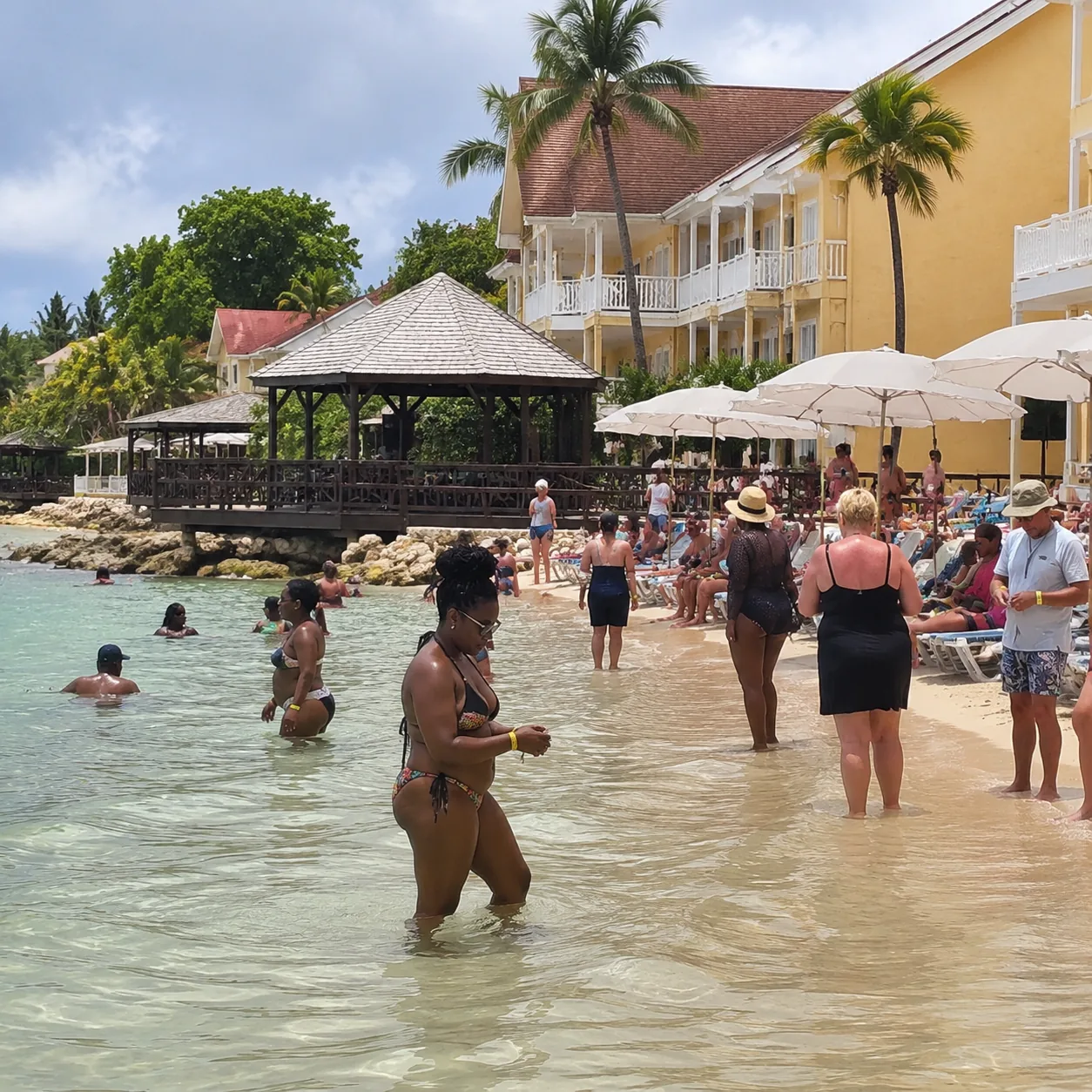 Square documentary travel photo of a Jamaica resort beach with shallow water, crowded loungers, resort buildings close t