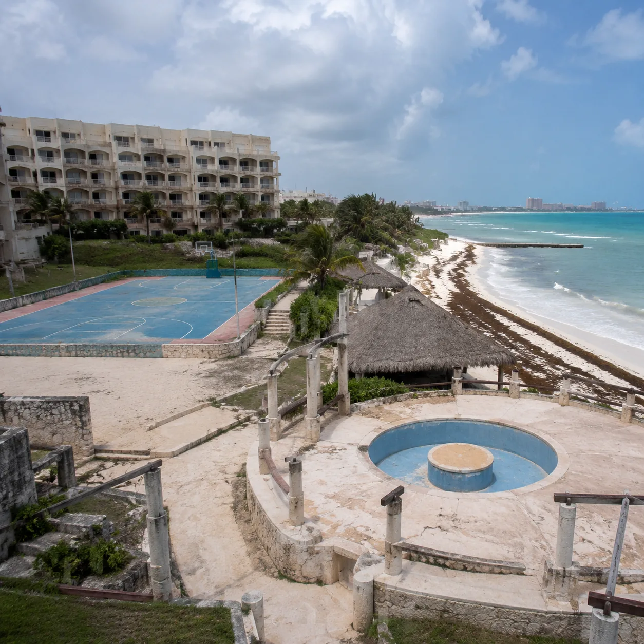 Square documentary travel photo of a faded Cancun all-inclusive resort with dated activity area, seaweed on the beach, e
