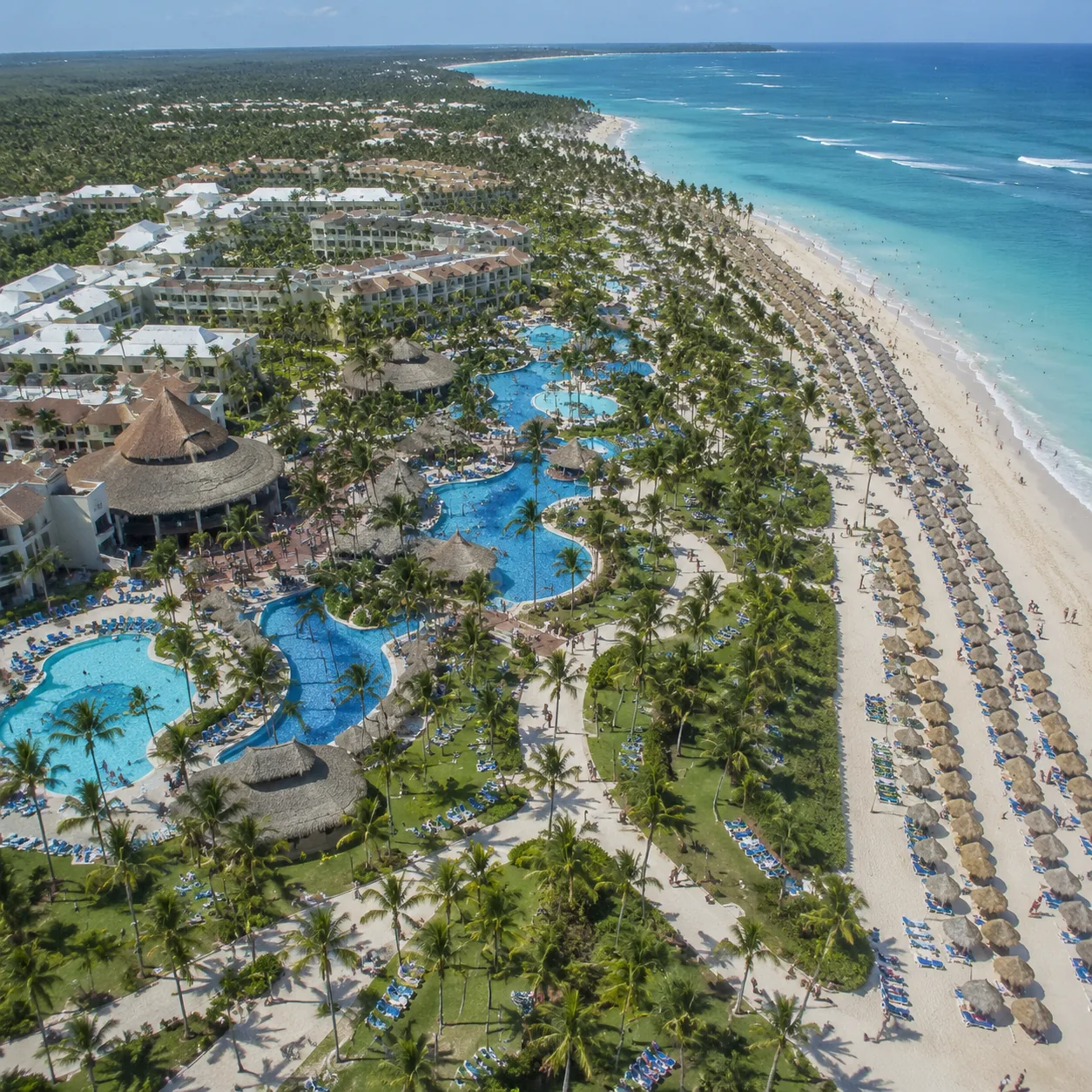 Square aerial-style travel photo of a massive Punta Cana resort complex with many pools, crowded paths, beach chairs lin