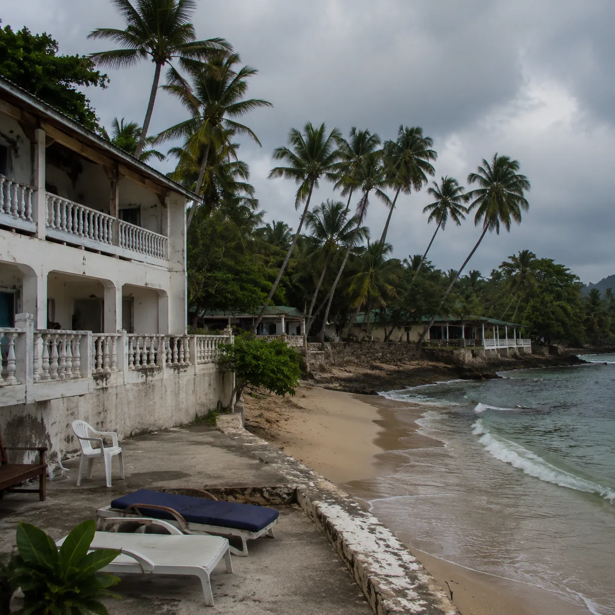 Square documentary travel photo of a run-down Tobago beach resort with basic rooms, small beach, aging furniture, cloudy