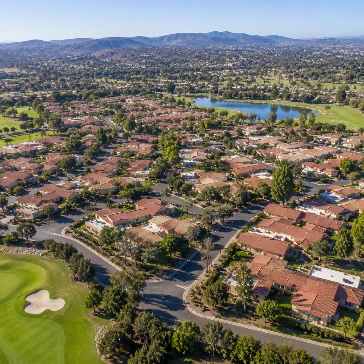 Realistic editorial photo of a large Orange County retirement village with dense low-rise buildings, golf course edges, 