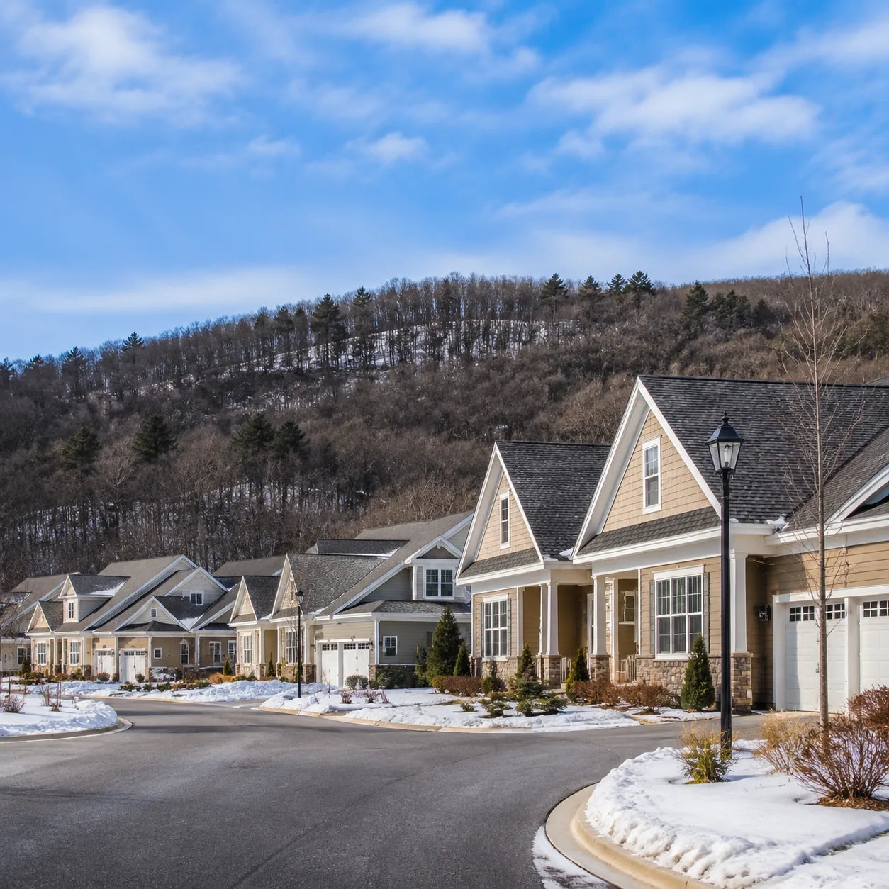 Realistic editorial photo of a Hudson Valley active adult community with townhomes, wooded hills, a cold blue sky, and s