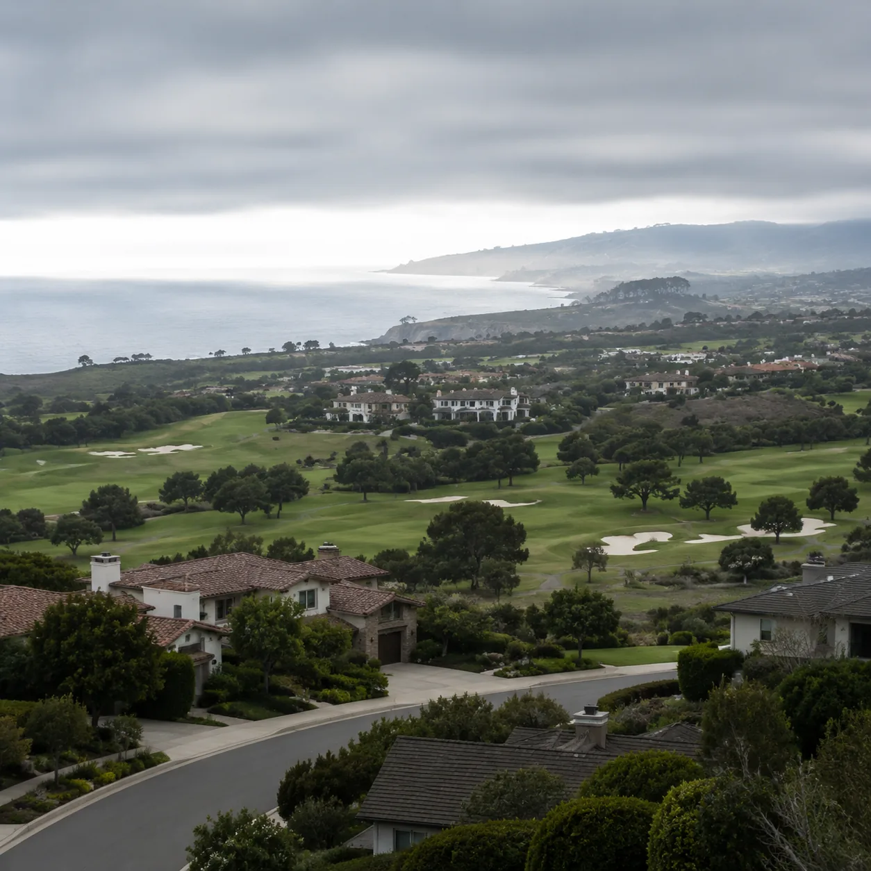 Realistic editorial photo of a Central Coast California golf community with coastal hills, neat homes, gray marine layer