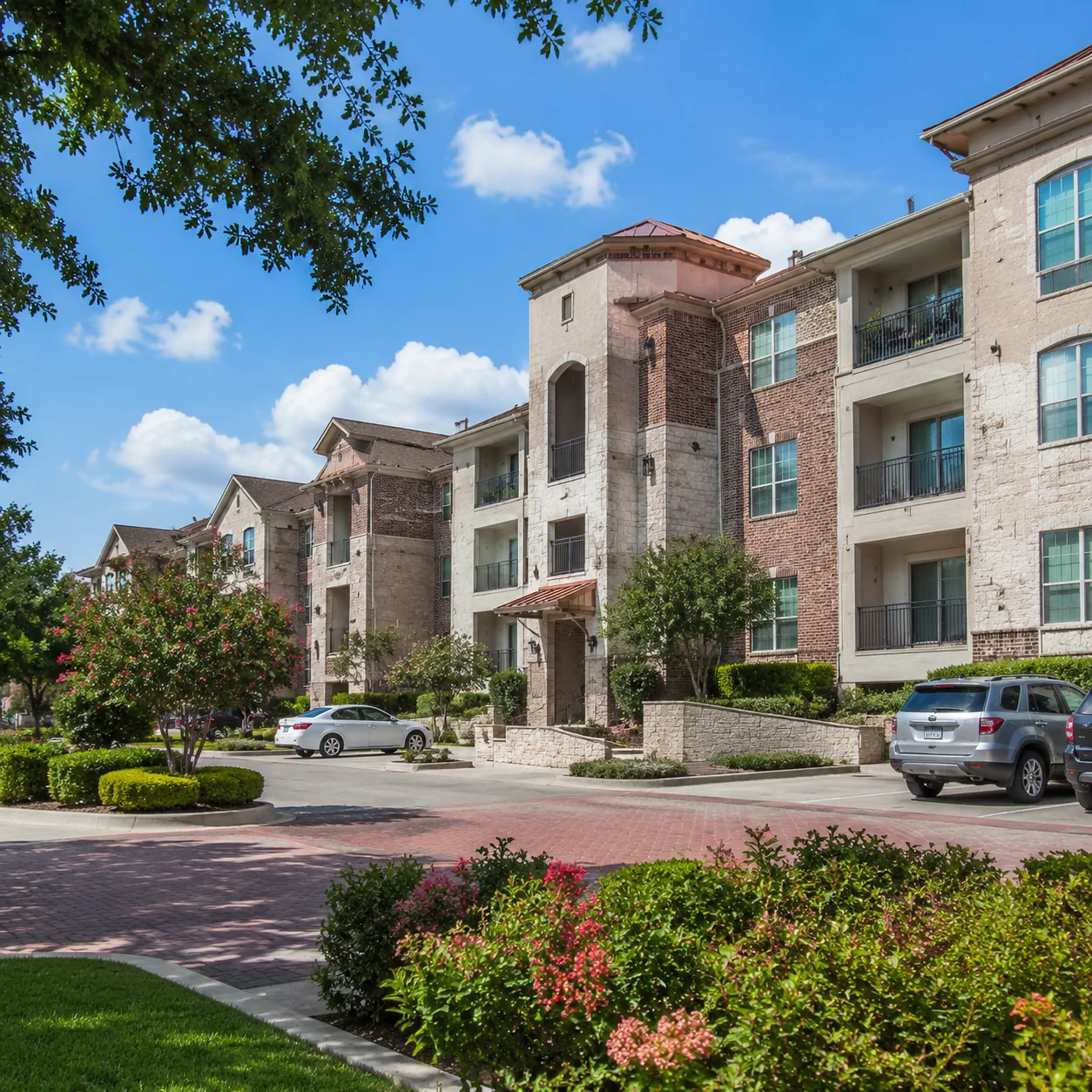 Realistic editorial photo of a Dallas-area 55 plus condo community with elevator buildings, parking, fresh landscaping, 