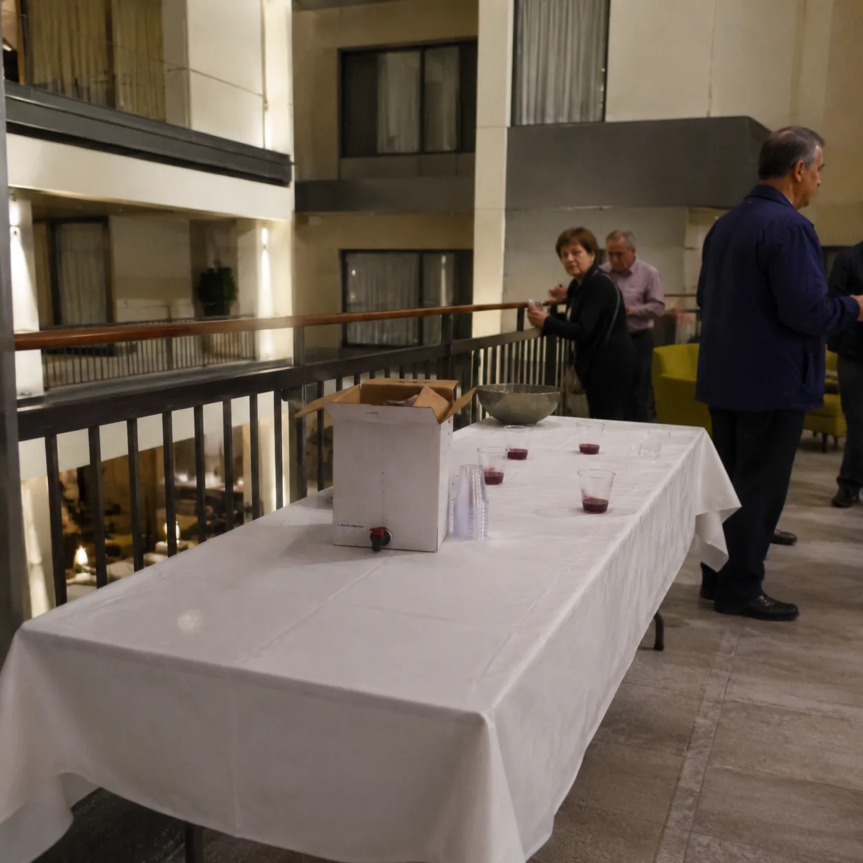 Sad hotel happy hour table in an atrium lounge, a box of wine and small plastic cups on a nearly empty banquet table, a 