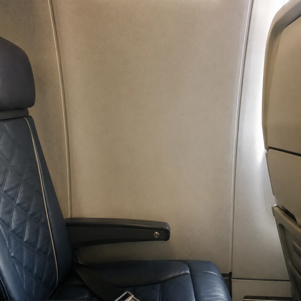 Realistic editorial photo of an airplane window seat beside a blank cabin wall panel where a window should be, realistic