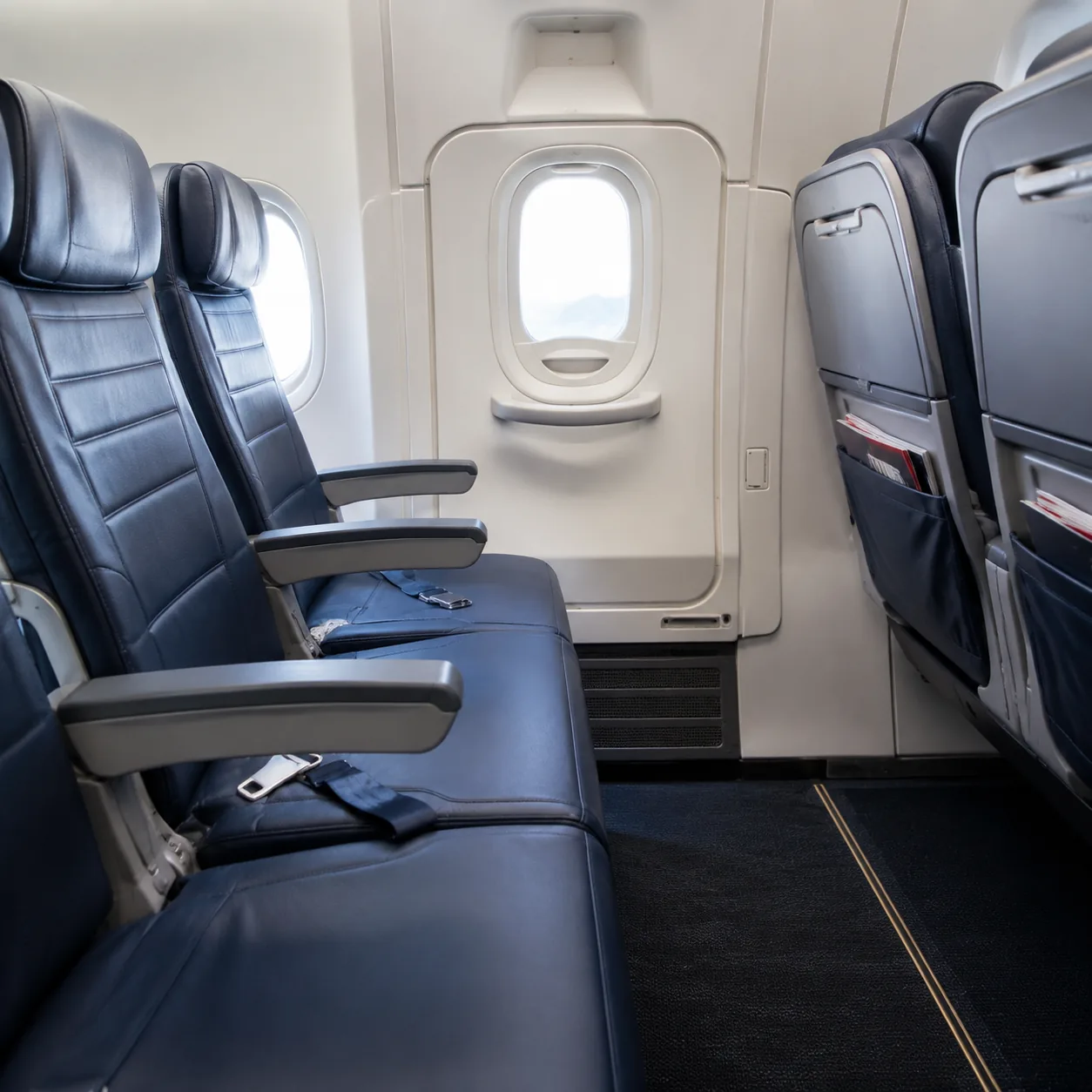 Realistic editorial photo of an airplane exit row seat with extra legroom and a closed emergency exit door nearby, reali