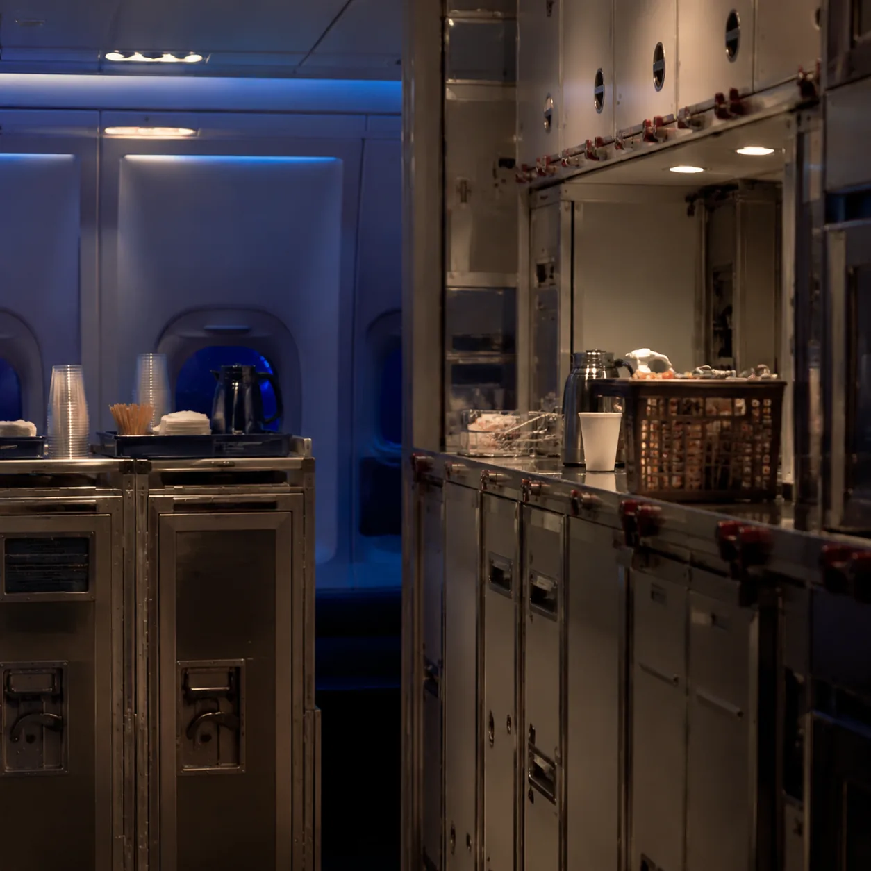 Realistic editorial photo of an airplane galley with service carts and soft cabin lighting during a night flight, realis