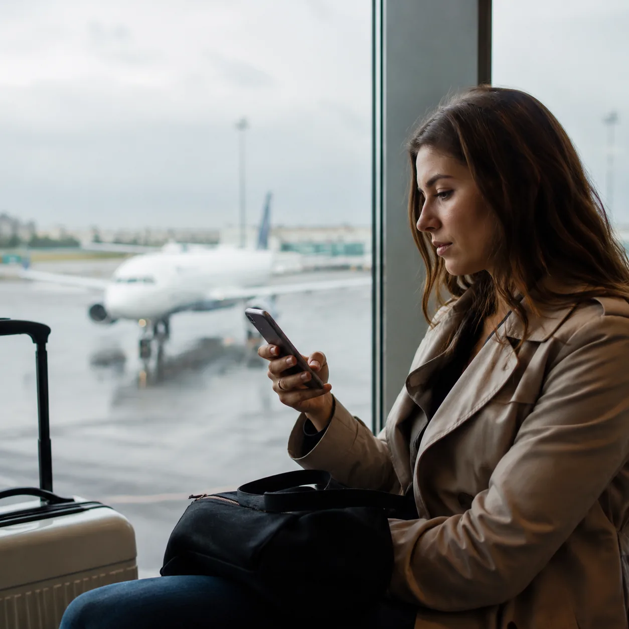 Realistic editorial photo of a traveler checking a flight app notification at an airport window with airplane outside, r