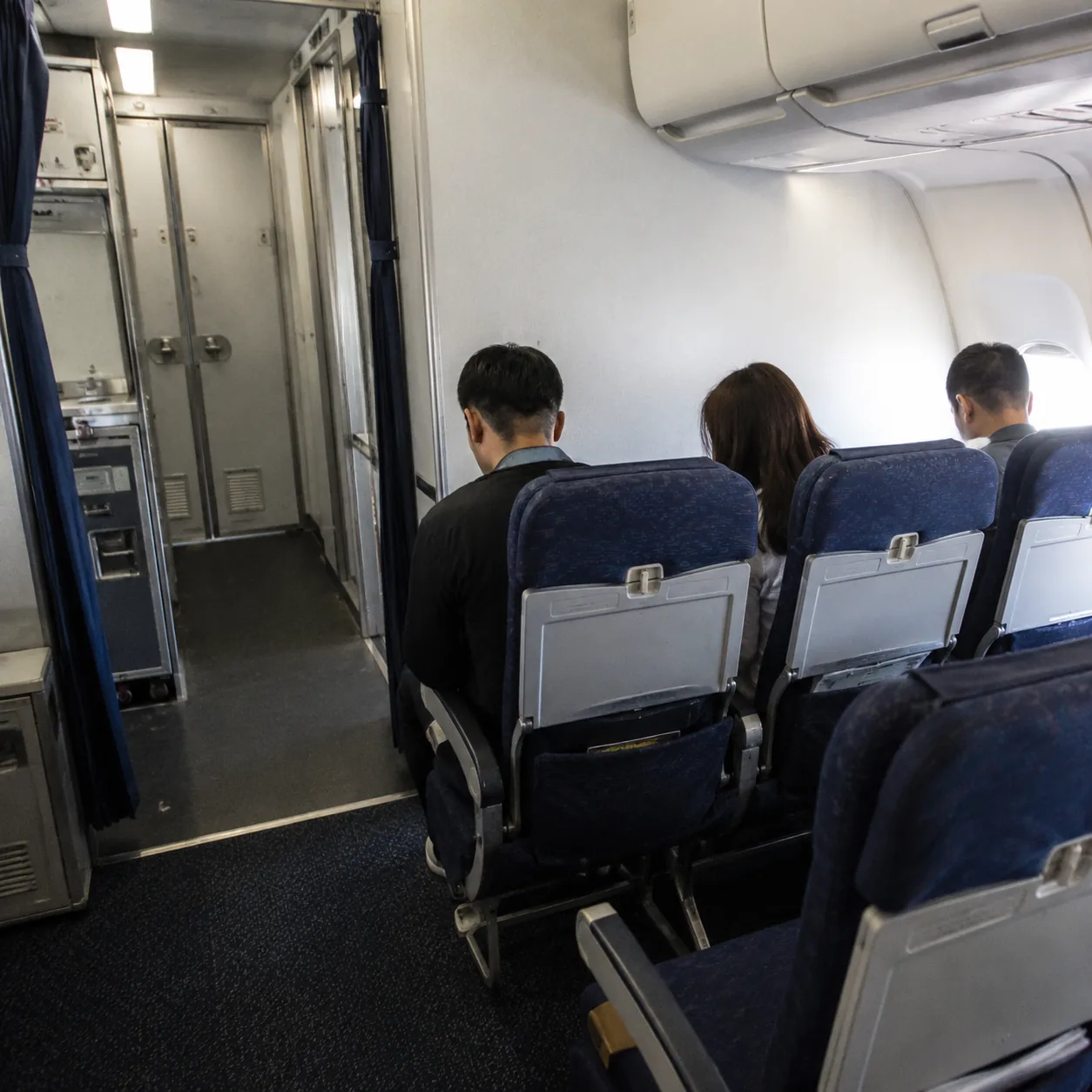 Realistic editorial photo of the last row of economy airplane seats near rear lavatory and galley area, realistic editor