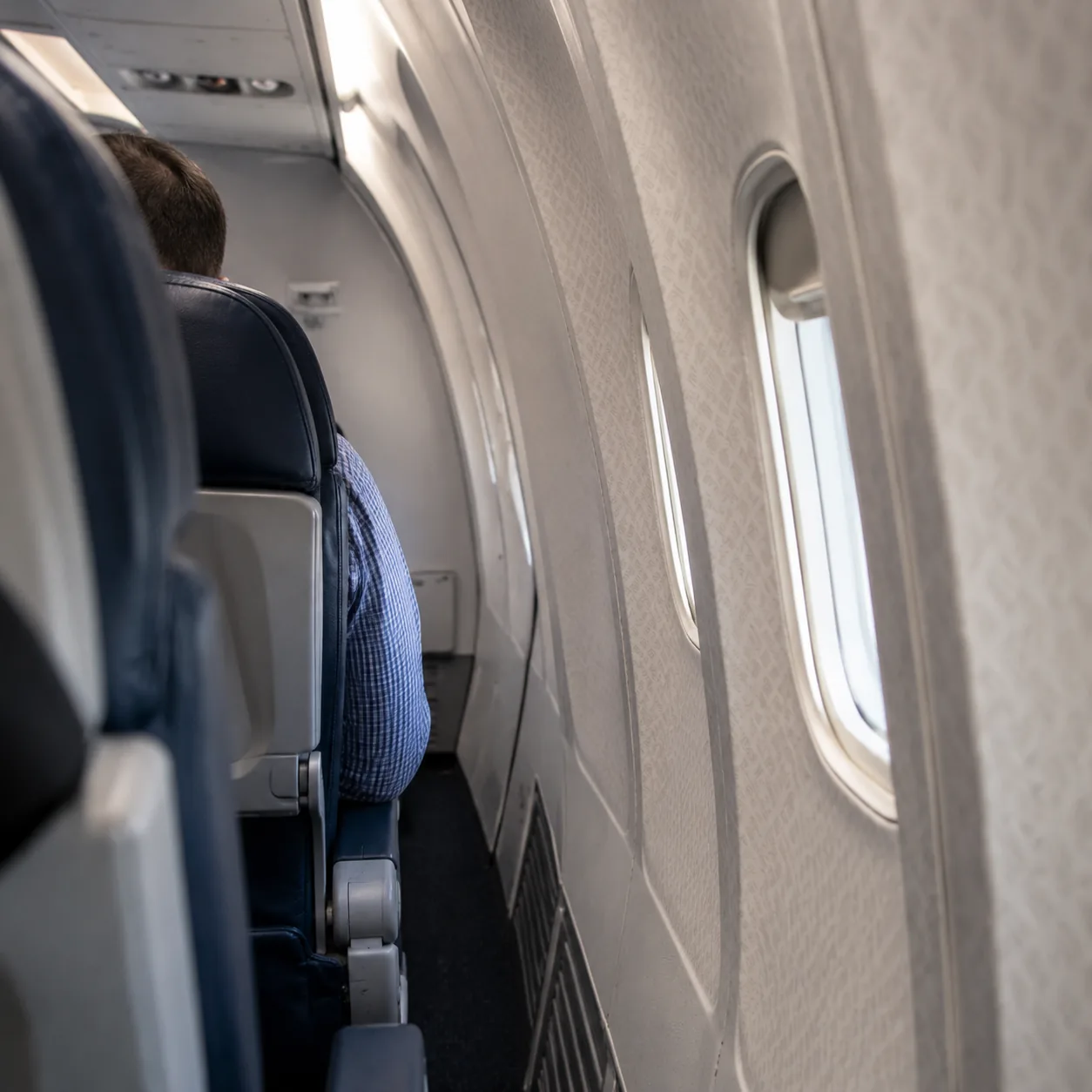 Realistic editorial photo of a narrow airplane cabin row near the rear where the cabin wall curves inward beside the win