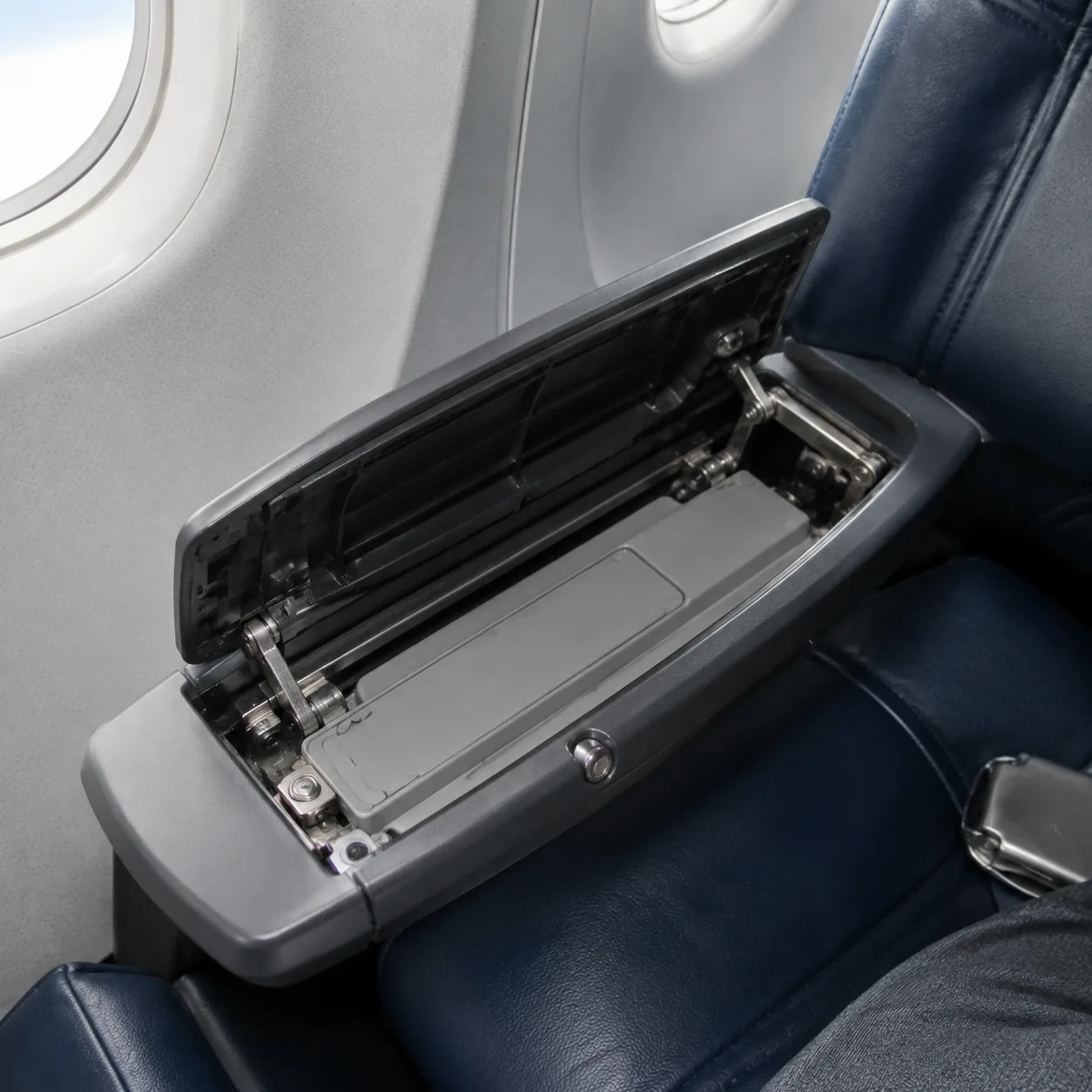 Realistic editorial photo of an airplane seat armrest opened to reveal a folded tray table mechanism, realistic editoria