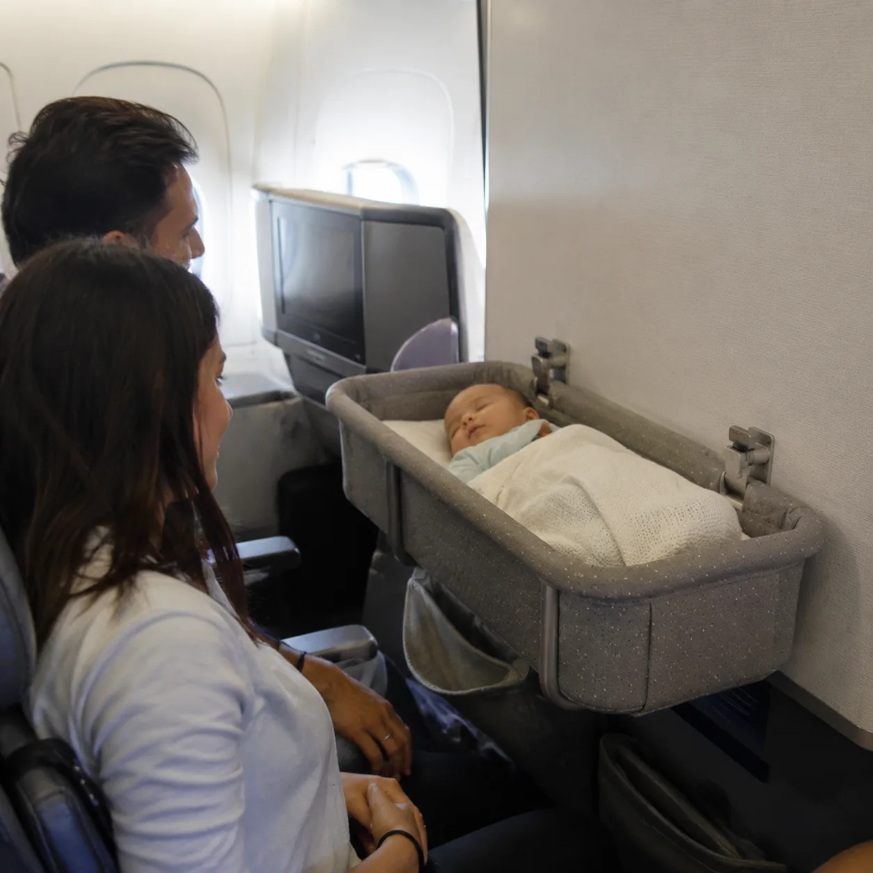 Realistic editorial photo of an airplane bulkhead bassinet position with nearby family seating area, realistic editorial