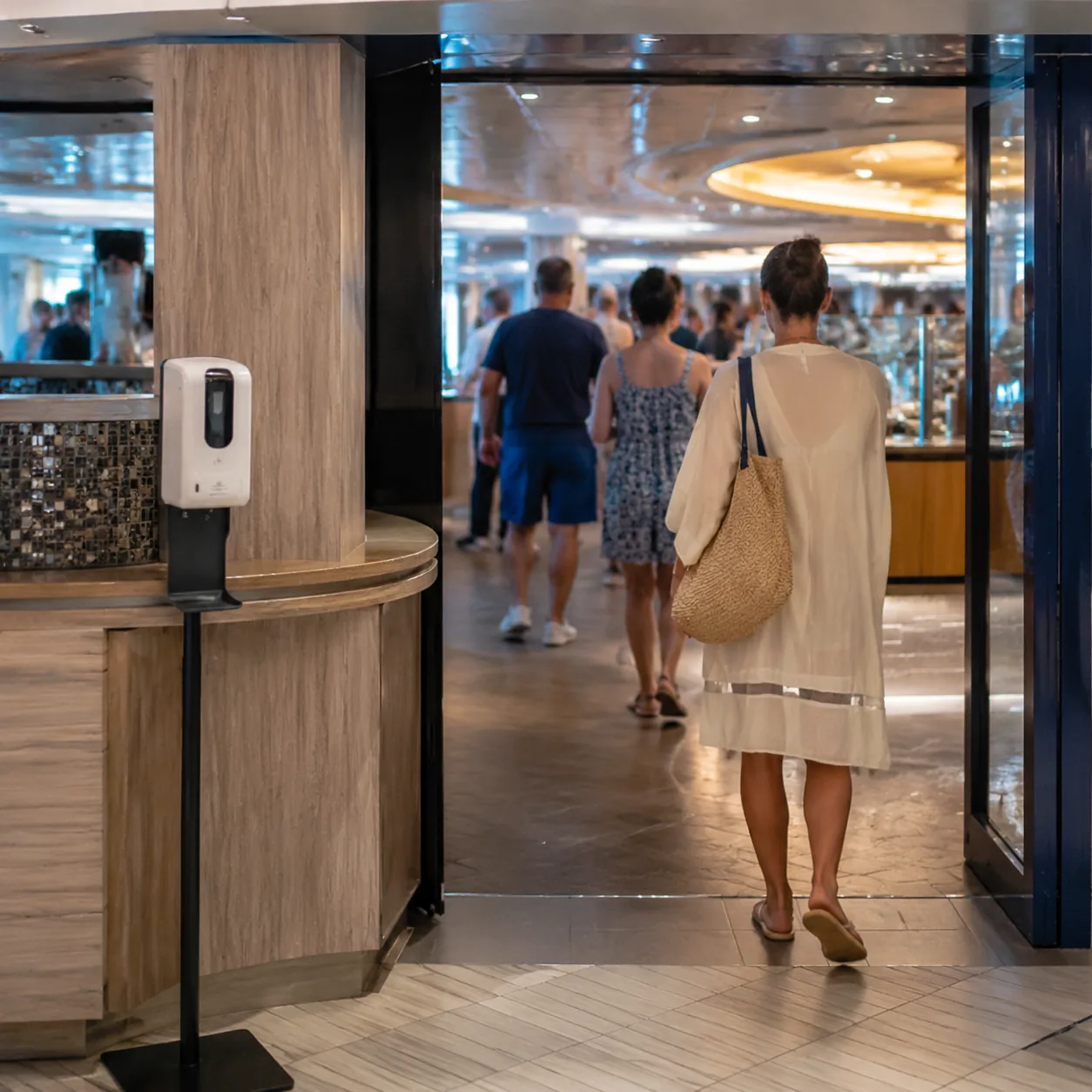 Realistic editorial photo of a cruise ship buffet entrance with hand sanitizer station and passengers entering dining ar