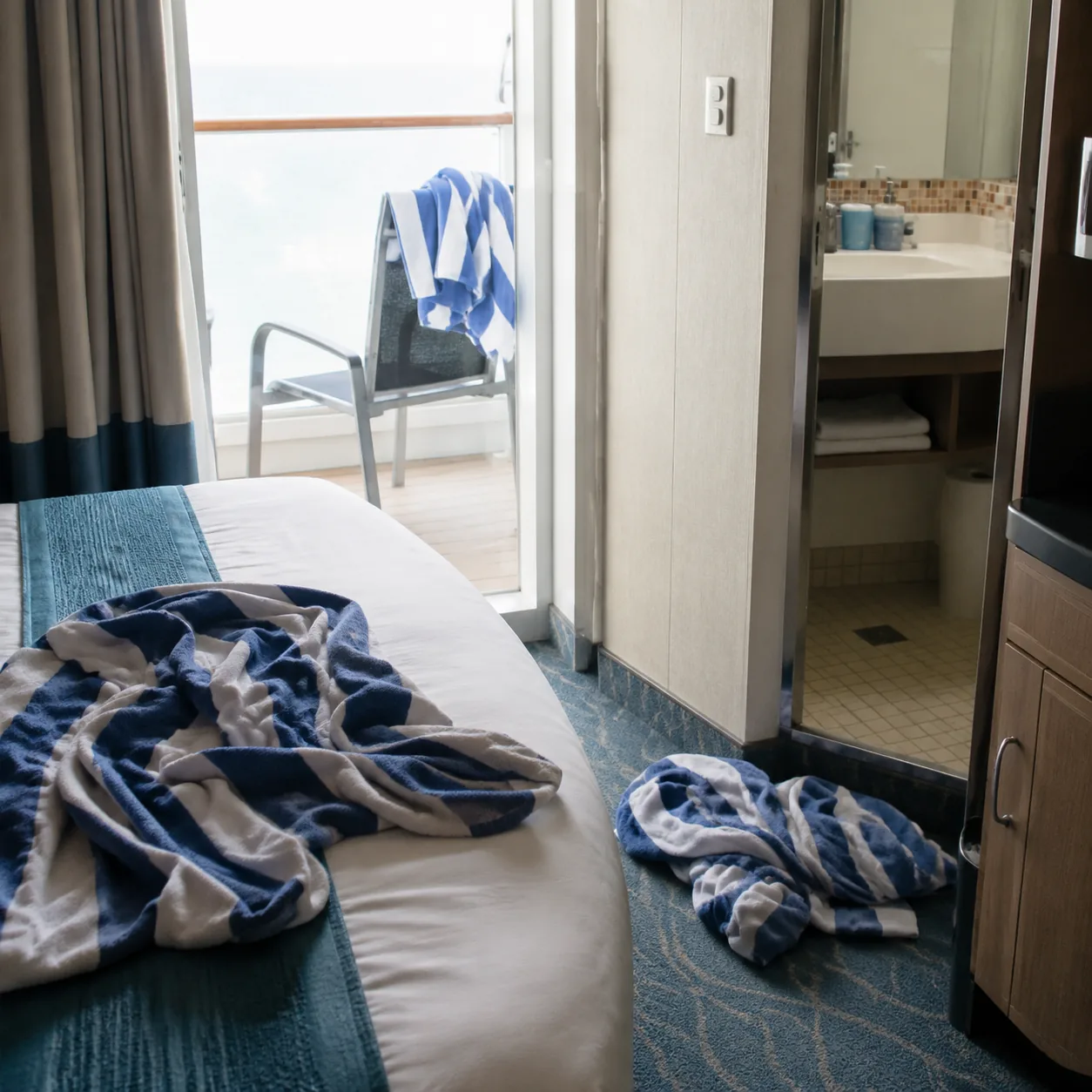Realistic editorial photo of damp cruise pool towels left on a cabin bed, balcony chair, and bathroom floor after a beac