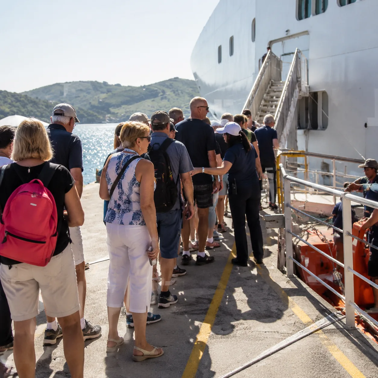 Realistic editorial photo of cruise passengers waiting for a tender boat near a ship gangway while crew organize the lin