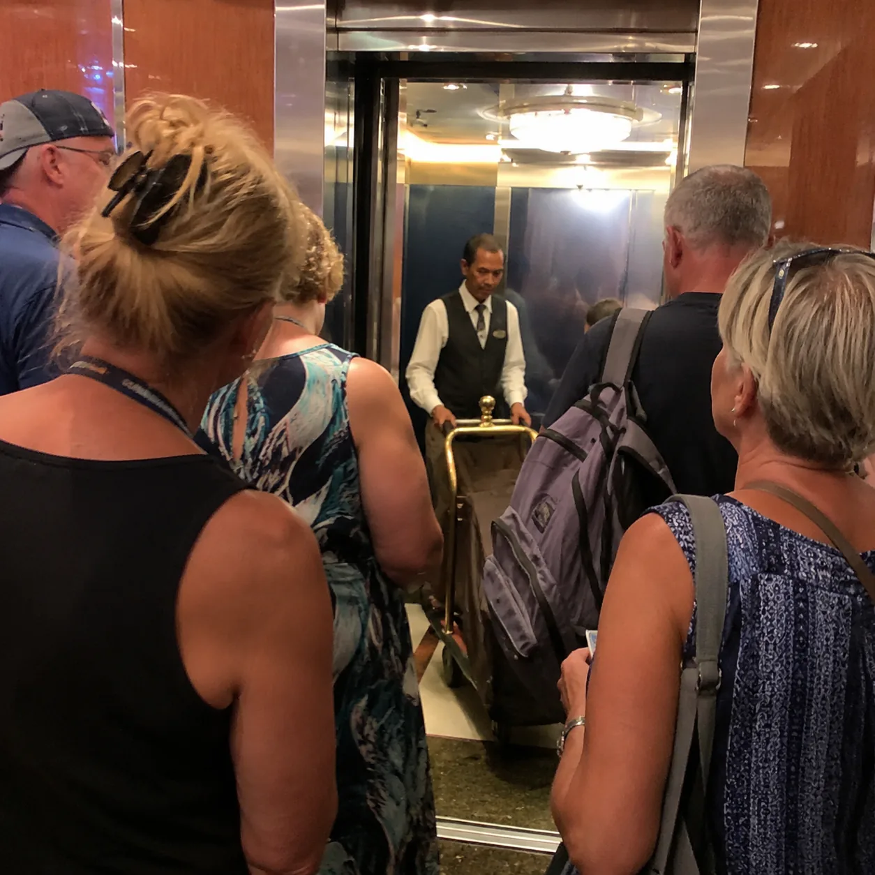 Realistic editorial photo of crowded cruise ship elevator lobby with passengers waiting too close to opening doors while