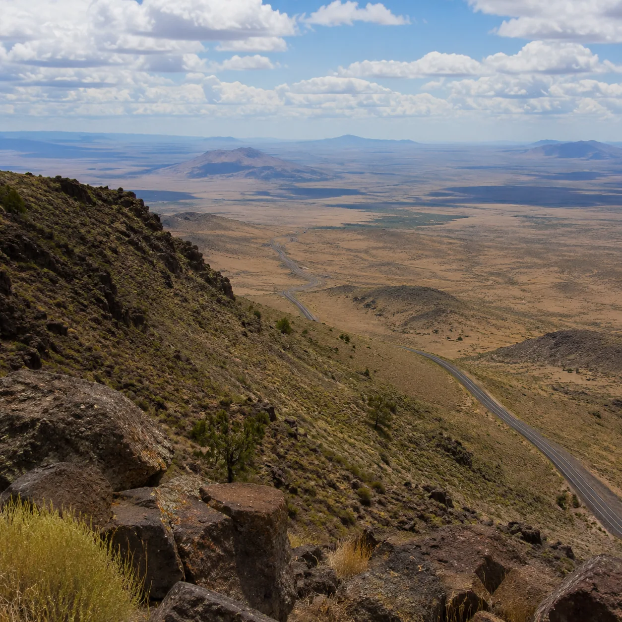Realistic editorial photo of vast overlook from Steens Mountain in Oregon across desert basin and empty road, warm natur