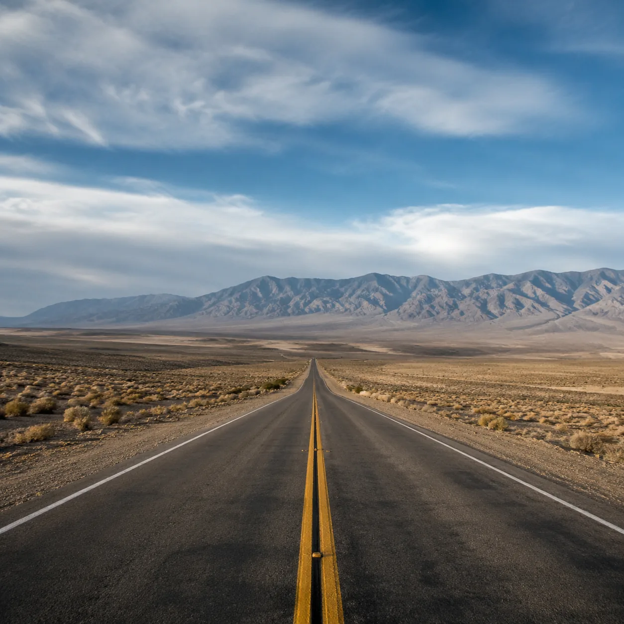 Realistic editorial photo of lonely two lane highway across central Nevada desert basin with mountains and huge sky, war